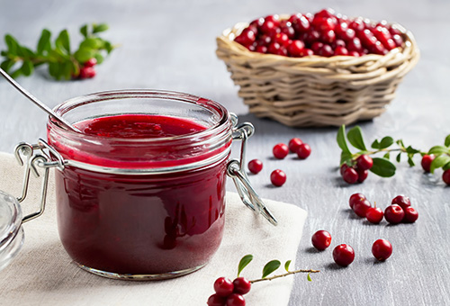 Preiselbeermarmelade Marmelade aus Preiselbeeren im Glas im Vordergrund, im Hintergrund ein Körbchen mit reifen Preiselbeeren