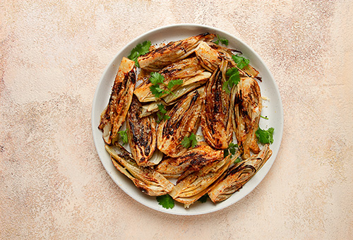 Ofenfenchel mit Blauschimmelkäse und Trauben Im Ofen gerösteter Fenchel auf einem weißen Teller vor einem apricotfarbenen Hintergrund