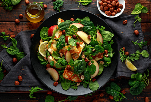 Sommersalat mit gegrilltem Halloumi und Pfirsich Sommersalat mit gegrilltem Halloumi und Pfirsich auf einem schwarzen Teller angerichtet