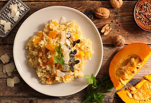 Kürbisrisotto auf weißem Teller, angerichtet mit Kürbiswürfel und Parmesanhobeln auf einem herbstlich dekorierten Tisch