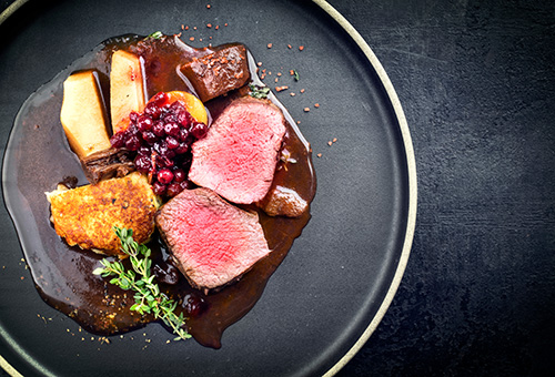 Hirschrücken mit Kartoffelpüree und Preiselbeeren in Rotwein-Sauce als Draufsicht auf einem Teller