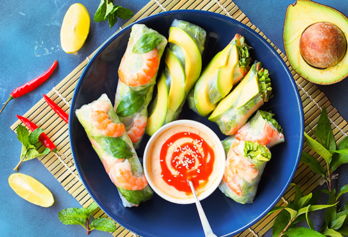 Sommerrollen mit Garnelen und Avocado und ein Sweet-Chili-Dip in einer blauen Schüssel