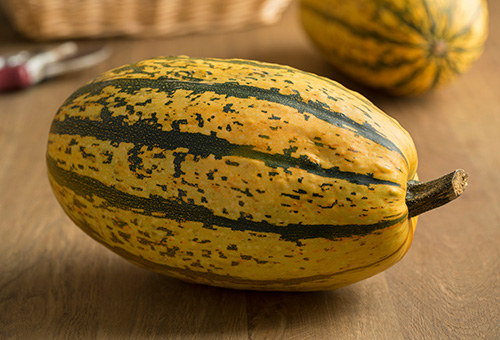 Ein ganzer Spaghettikürbis auf einem Holztisch, im Hintergrund sieht man noch einen Spaghettikürbis