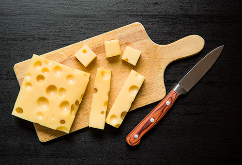 Block Schnittkäse und Käsewürfel auf einem Holzbrett drapiert