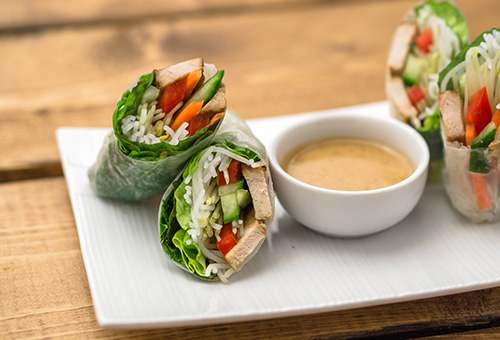 Vegane Sommerrollen mit Tofu auf einem weißen Teller und ein Erdnuss-Dip in einem weißen Schälchen