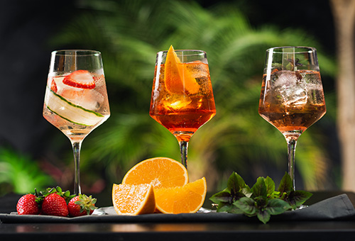 Verschiedene Spritz-Varianten Drei verschiedene Spritz-Varianten mit Dekoration auf einem Tisch
