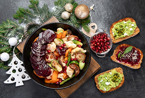Veganes Weihnachtsessen mit Roter Bete, Rosenkohl, Pilzen, Blumenkohl, Spargel und Granatapfel in einer schwarzen Schüssel auf einem festlich dekorierten Tisch