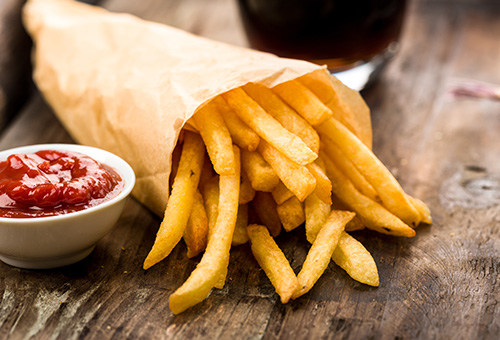 Pommes in Papiertüte mit Ketchup in Schälchen auf Holztisch