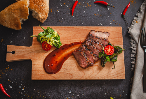 Geschnittenes Nackensteak vom Wildschwein serviert auf einem Holzbrett, daneben gestrichener Chipotle Ketchup