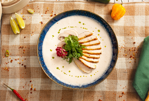 Rezept: Tom Kha Gai mit Perlhuhnbrust, Pilzen und Thai-Basilikum Geschnittene Perlhuhnbrust liegt auf einer Tom Kha Gai Suppe