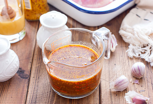 Frische Honig-Senf Marinade in einem kleinen Glas auf einem Holztisch mit Zutaten wie Knoblauch und Salz drumherum