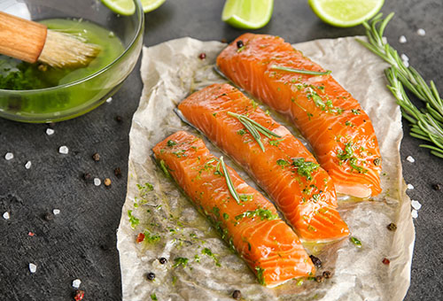 Mit Kräutermarinade bestrichene frische Lachsfiletstreifen auf Pergamentpapier