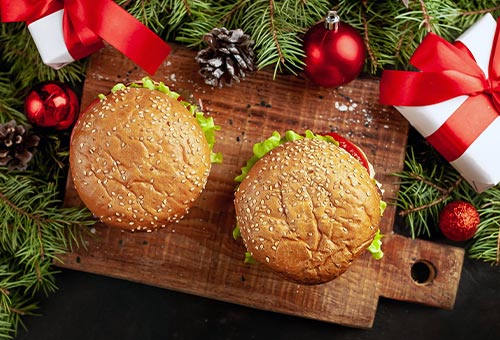 zwei Burger auf einem Holzbrett mit Weihnachtsdeko und kleinen Geschenken