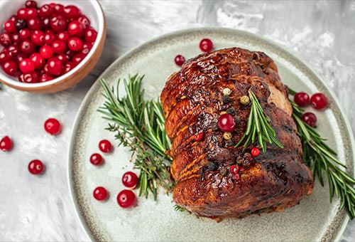 Spanferkel Rollbraten auf einem hellen Teller angerichtet und garniert mit Rosmarin und Cranberries.