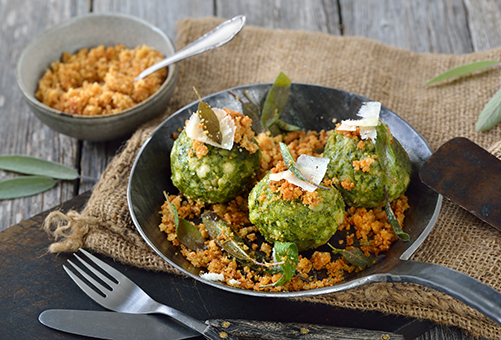 Vegetarische Spinatknödel - Hausmannskost Drei vegetarische Spinatknödel in einer Gusspfanne angerichtet mit Röstzwiebeln in einer Gusspfanne.