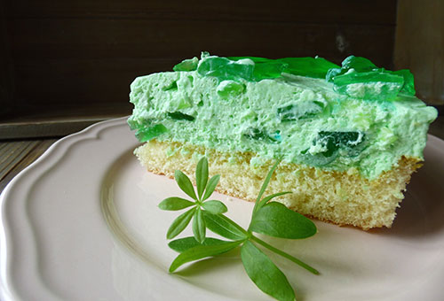 Ein Stück Waldmeister-Philadelphia Torte mit Götterspeise auf einem weißen Teller.