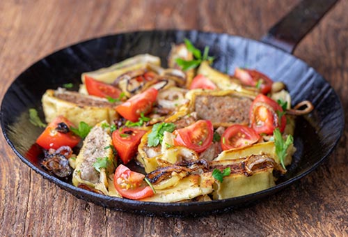Schwäbische Maultaschen Maultaschenscheiben angebraten mit kleinen Tomaten und Zwiebeln in einer Gusspfanne garniert mit frischen Kräutern