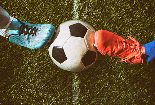 Gastronomie Quiz Fußball EM Zwei Fußballstollenschuhe die einen Ball auf dem Rasen stoppen.