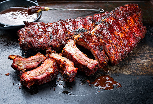 Verschiedene Spareribs-Stücke liegen auf einer Platte mit einer Soße daneben