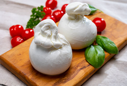 Frischer Burrata auf einem Holzbrett mit Kirschtomaten und Basilikumblättern angerichtet.
